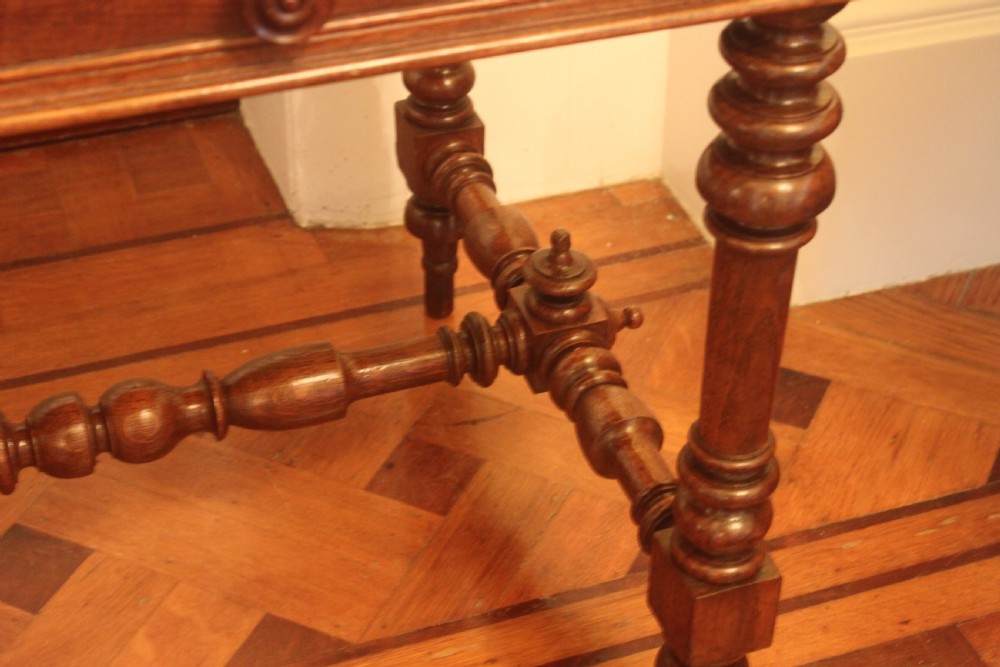 An antique French oak writing desk featuring a gold-tooled dark leather top insert, frieze drawers, turned baluster legs, and a stretcher base with a central finial. View IX