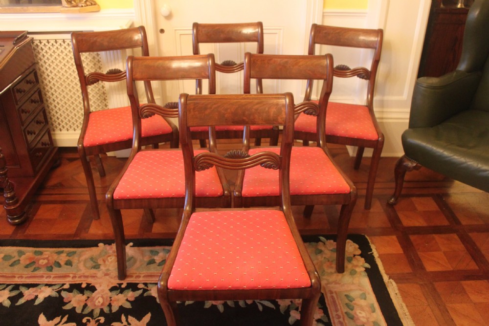A set of six Regency mahogany dining chairs featuring carved crest rails and red patterned upholstered seats.