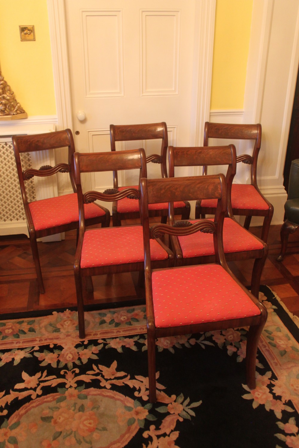 A set of six Regency mahogany dining chairs featuring carved crest rails and red patterned upholstered seats. View II