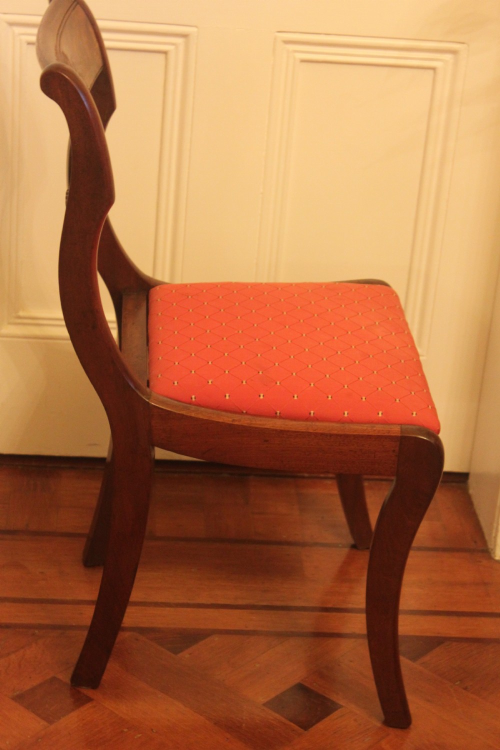 A set of six Regency mahogany dining chairs featuring carved crest rails and red patterned upholstered seats. View V