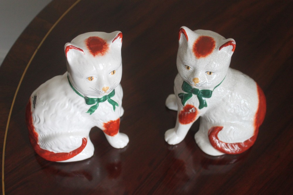 A pair of white press-moulded earthenware cat figurines featuring hand-painted rust-red patches and green ribbon bow collars. View III