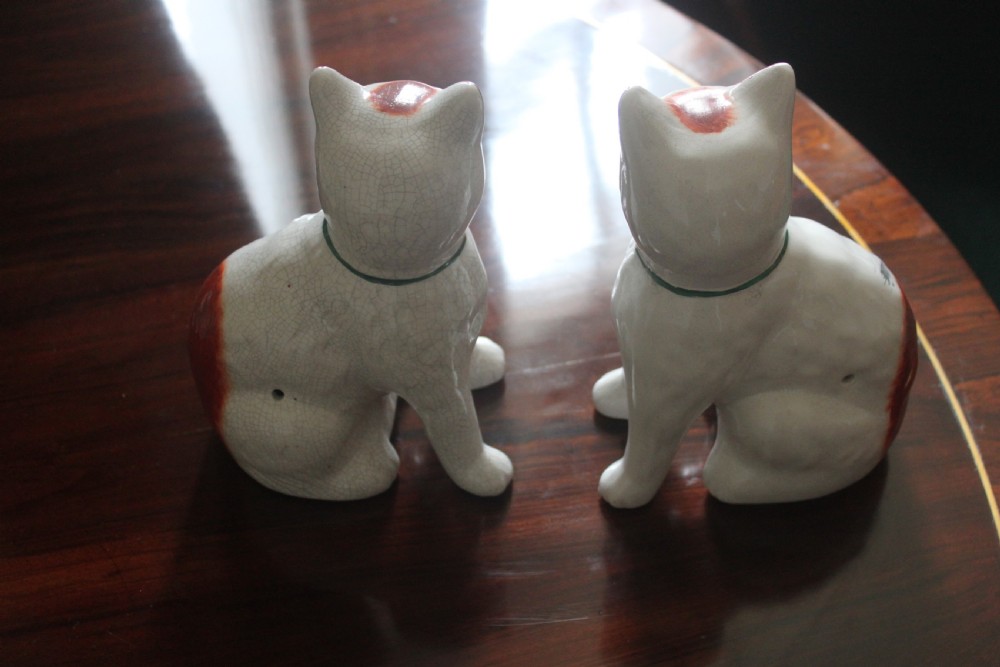 A pair of white press-moulded earthenware cat figurines featuring hand-painted rust-red patches and green ribbon bow collars. View VI