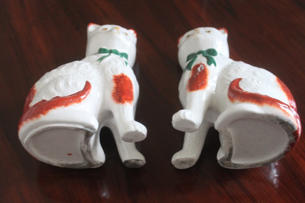 A pair of white press-moulded earthenware cat figurines featuring hand-painted rust-red patches and green ribbon bow collars. View VII