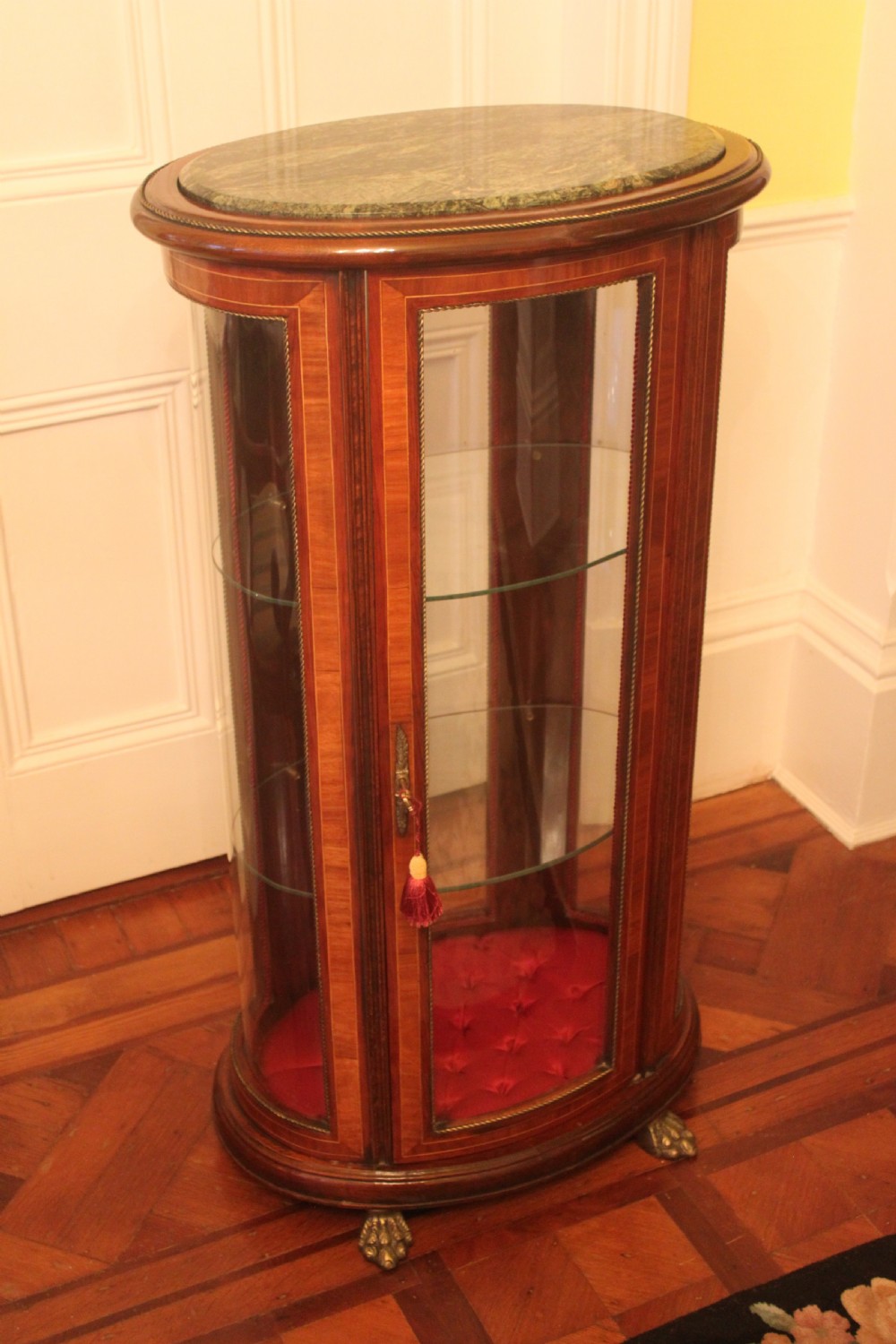 An oval antique French vitrine cabinet featuring an inset green marble top, inlaid timber marquetry, curved glass panels, and brass claw feet. View II