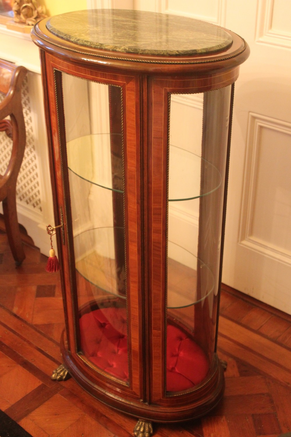 An oval antique French vitrine cabinet featuring an inset green marble top, inlaid timber marquetry, curved glass panels, and brass claw feet. View III