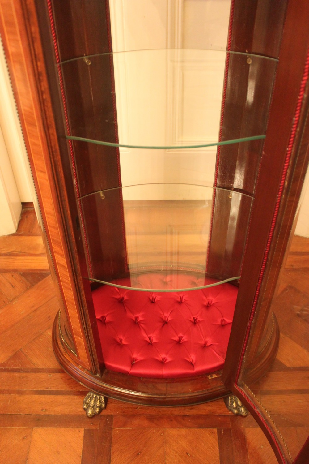 An oval antique French vitrine cabinet featuring an inset green marble top, inlaid timber marquetry, curved glass panels, and brass claw feet. View VI