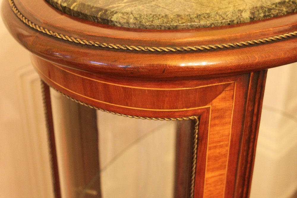 An oval antique French vitrine cabinet featuring an inset green marble top, inlaid timber marquetry, curved glass panels, and brass claw feet. View VII
