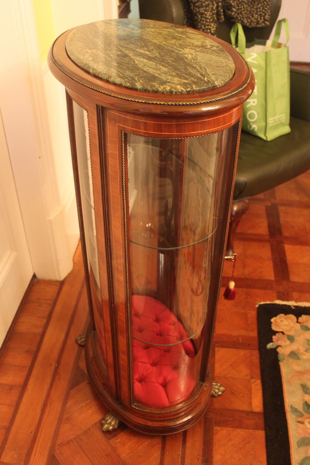 An oval antique French vitrine cabinet featuring an inset green marble top, inlaid timber marquetry, curved glass panels, and brass claw feet. View VIII