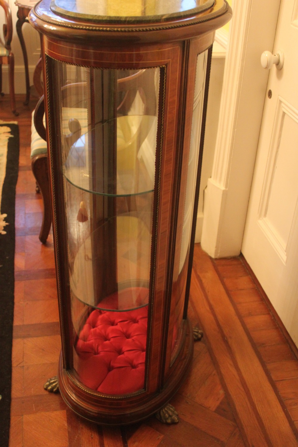 An oval antique French vitrine cabinet featuring an inset green marble top, inlaid timber marquetry, curved glass panels, and brass claw feet. View IX