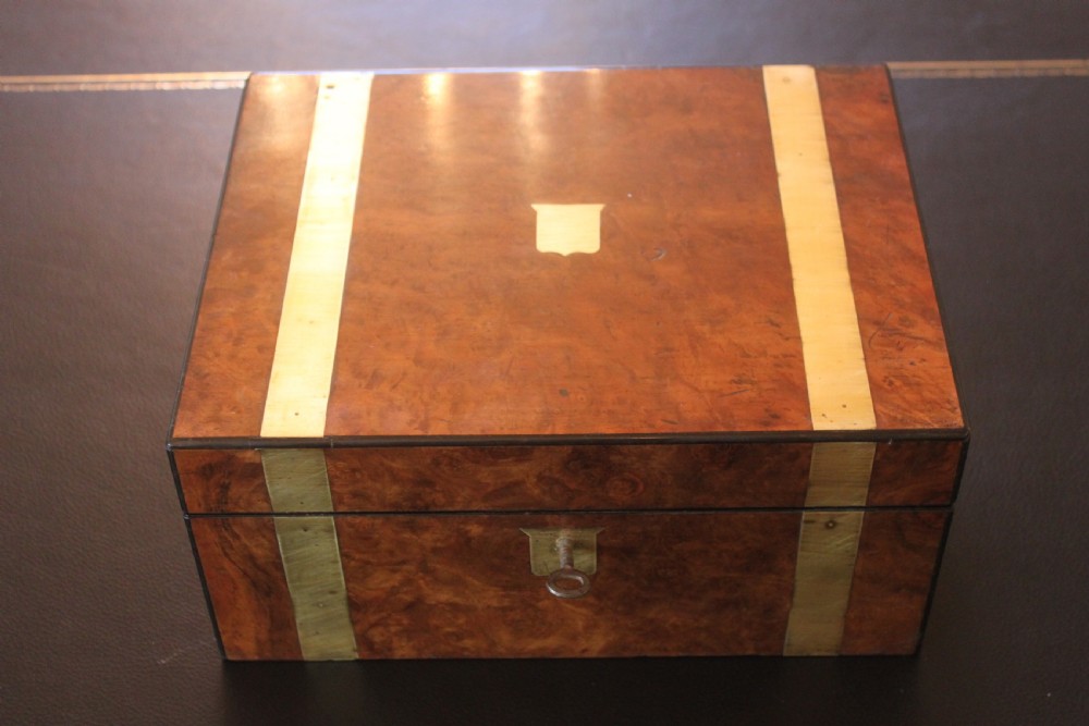 A closed rectangular Victorian burr walnut writing slope decorated with two wide brass straps and a central brass shield inlay.