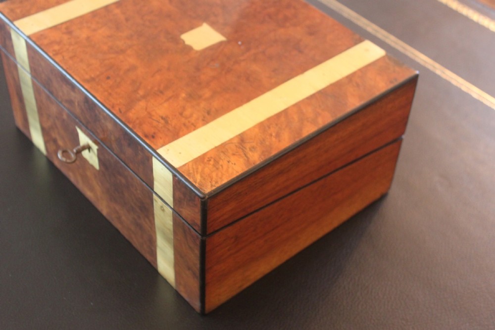 A closed rectangular Victorian burr walnut writing slope decorated with two wide brass straps and a central brass shield inlay. View II