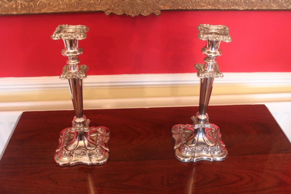 A pair of Victorian silver-plated candlesticks with ornate scroll motifs on square bases and tapered stems.