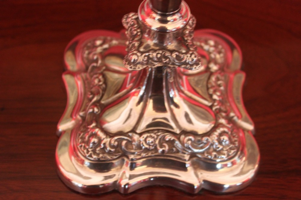 A pair of Victorian silver-plated candlesticks with ornate scroll motifs on square bases and tapered stems. View II