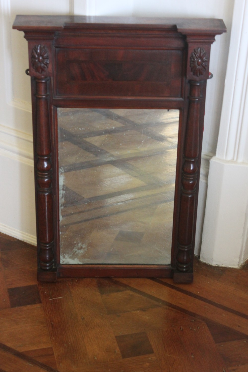 A George IV mahogany pier mirror featuring turned side columns, carved rosettes, a stepped cornice, and an aged glass plate.