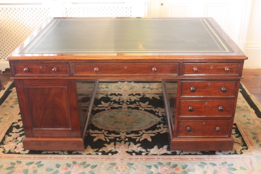 A Victorian mahogany partners desk featuring a green gilded leather writing surface and pedestals with turned wooden drawer knobs.