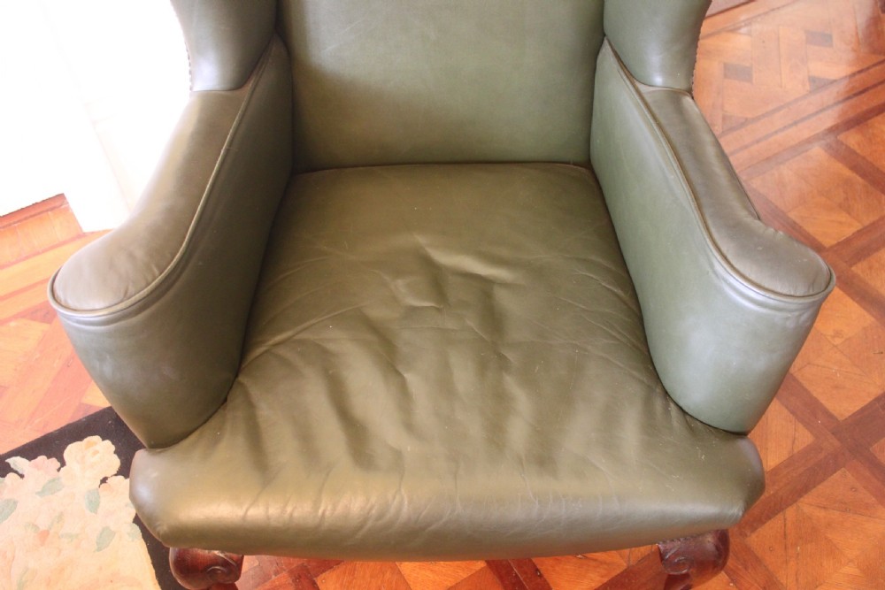 A late nineteenth or early twentieth century Queen Anne style wingback armchair upholstered in olive green leather with carved cabriole legs. View II