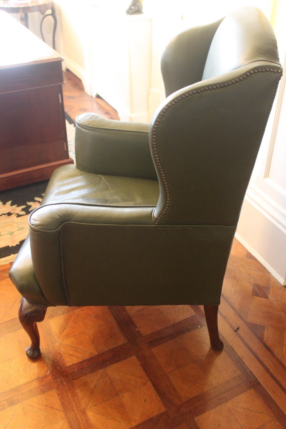 A late nineteenth or early twentieth century Queen Anne style wingback armchair upholstered in olive green leather with carved cabriole legs. View III