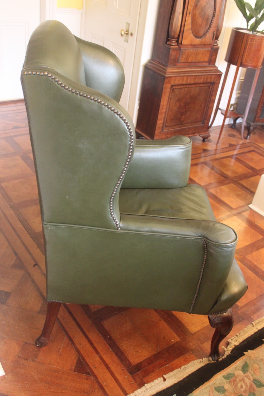 A late nineteenth or early twentieth century Queen Anne style wingback armchair upholstered in olive green leather with carved cabriole legs. View IV