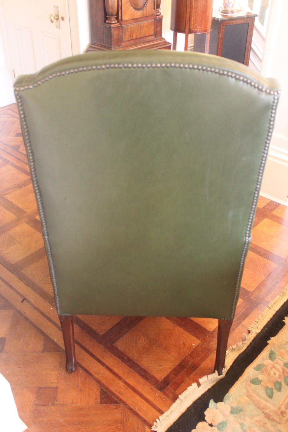A late nineteenth or early twentieth century Queen Anne style wingback armchair upholstered in olive green leather with carved cabriole legs. View V
