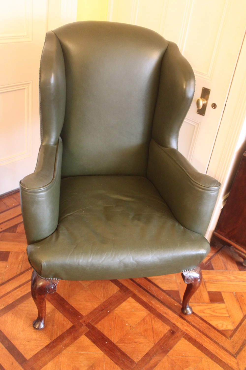 A late nineteenth or early twentieth century Queen Anne style wingback armchair upholstered in olive green leather with carved cabriole legs. View VI
