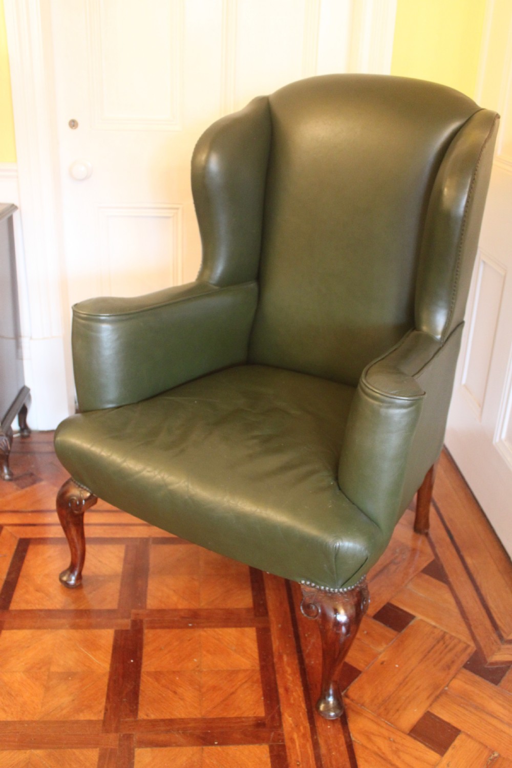 A late nineteenth or early twentieth century Queen Anne style wingback armchair upholstered in olive green leather with carved cabriole legs. View VII