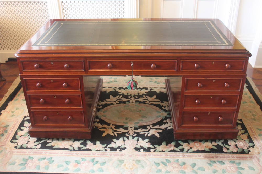 A Victorian mahogany partners desk featuring a dark leather writing insert, multiple pedestal drawers with turned wooden knobs, and a central frieze drawer.