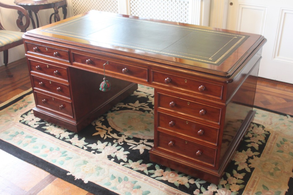 A Victorian mahogany partners desk featuring a dark leather writing insert, multiple pedestal drawers with turned wooden knobs, and a central frieze drawer. View V