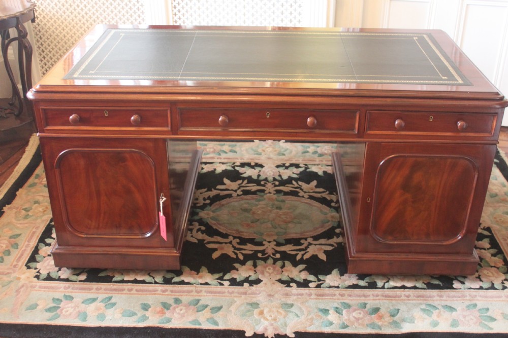A Victorian mahogany partners desk featuring a dark leather writing insert, multiple pedestal drawers with turned wooden knobs, and a central frieze drawer. View XII