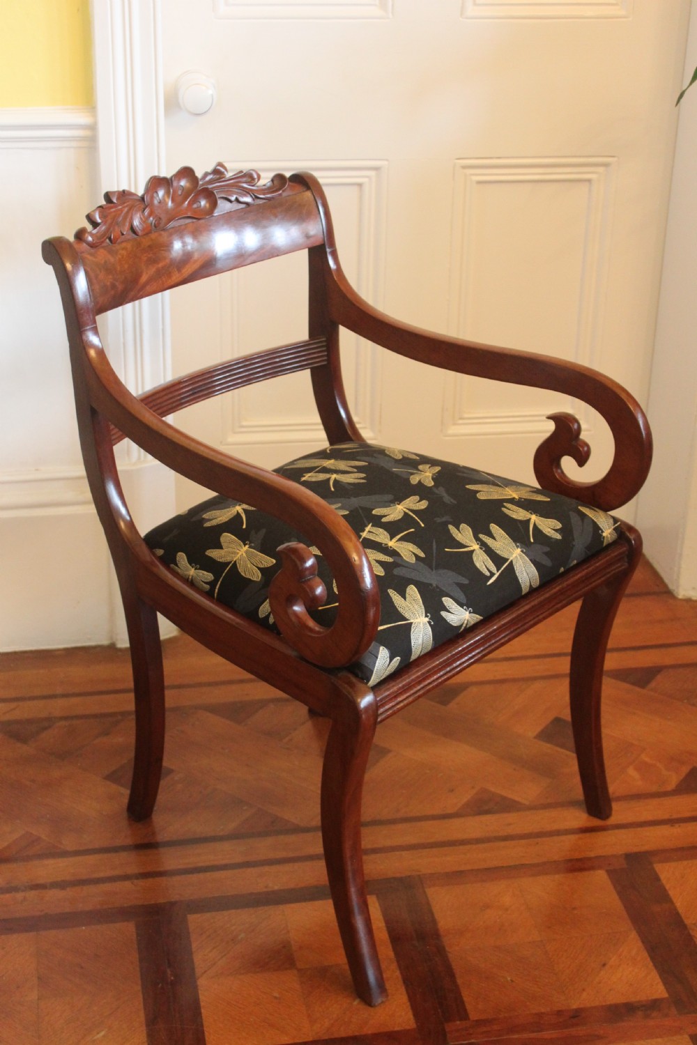 A Regency mahogany armchair featuring a carved crest rail, scrolled reeded arms, sabre front legs, and dragonfly pattern upholstery. View II