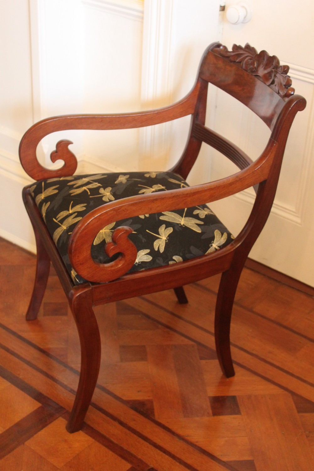A Regency mahogany armchair featuring a carved crest rail, scrolled reeded arms, sabre front legs, and dragonfly pattern upholstery. View III