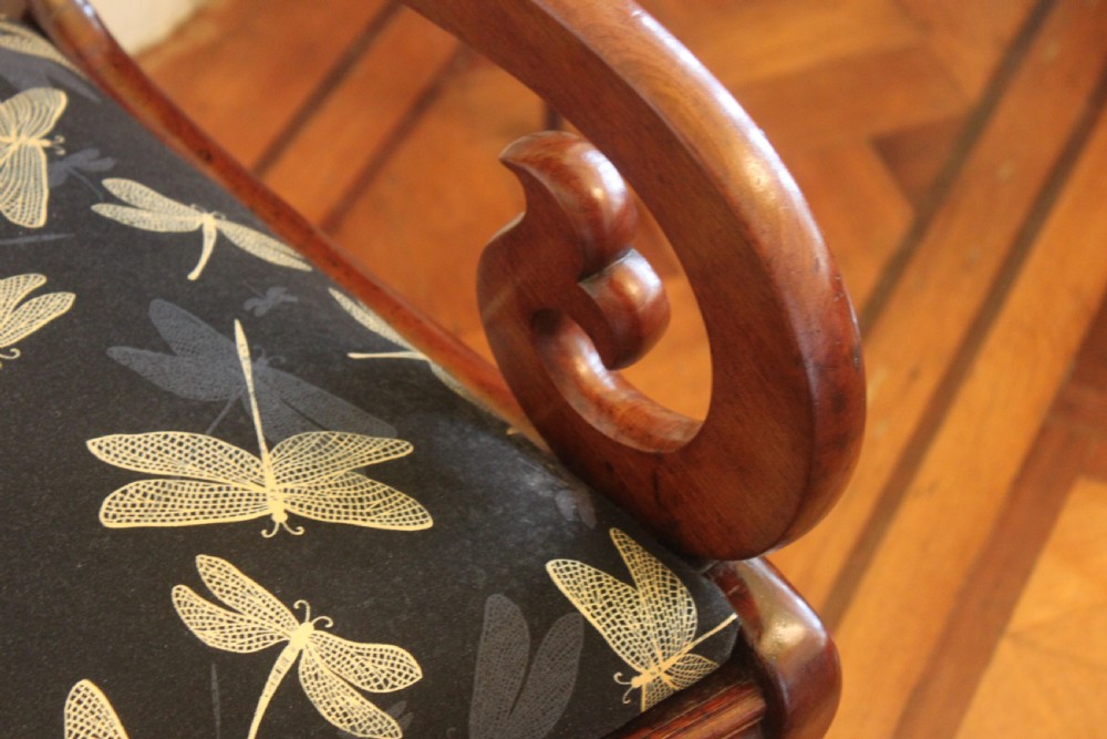 A Regency mahogany armchair featuring a carved crest rail, scrolled reeded arms, sabre front legs, and dragonfly pattern upholstery. View V