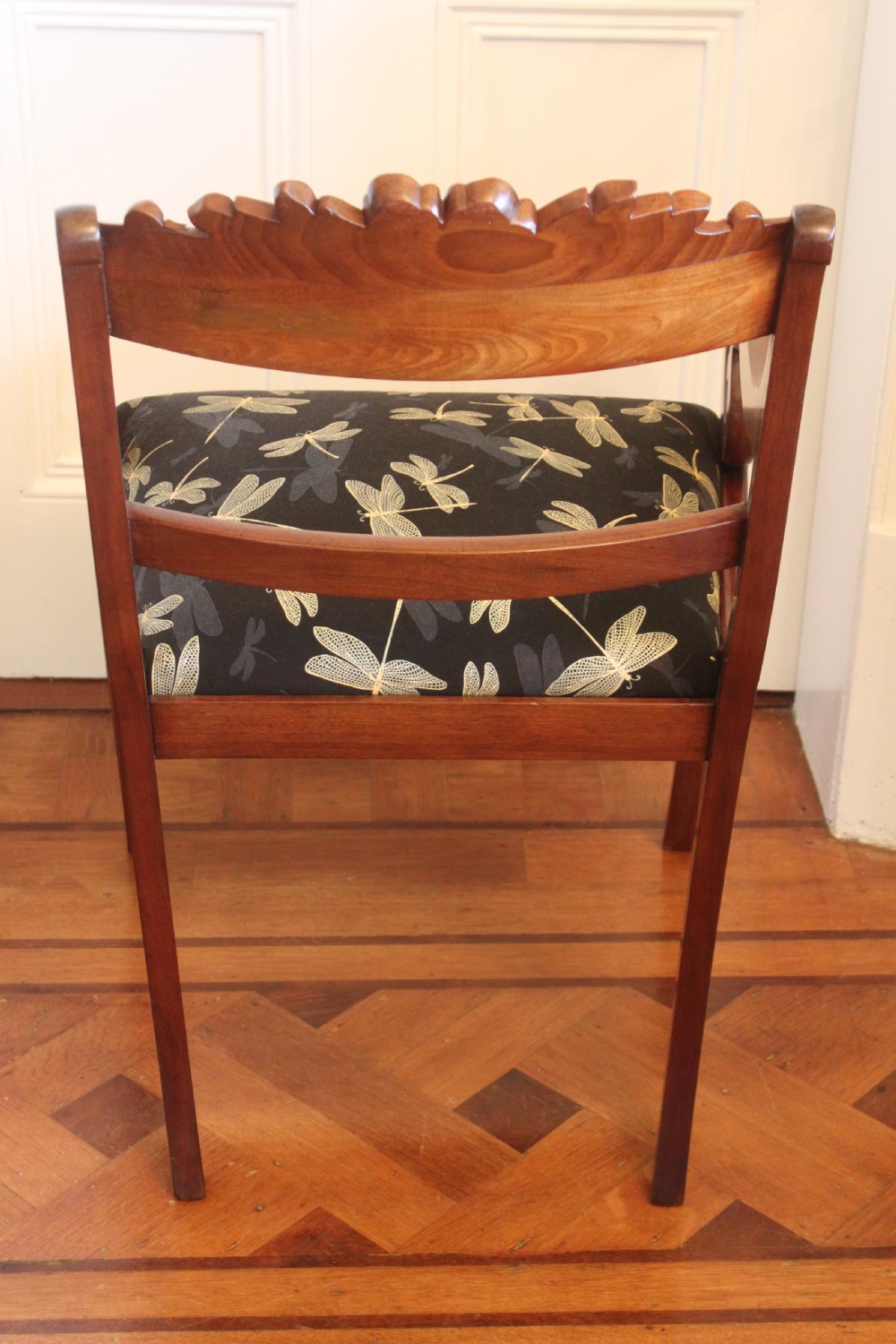 A Regency mahogany armchair featuring a carved crest rail, scrolled reeded arms, sabre front legs, and dragonfly pattern upholstery. View VI