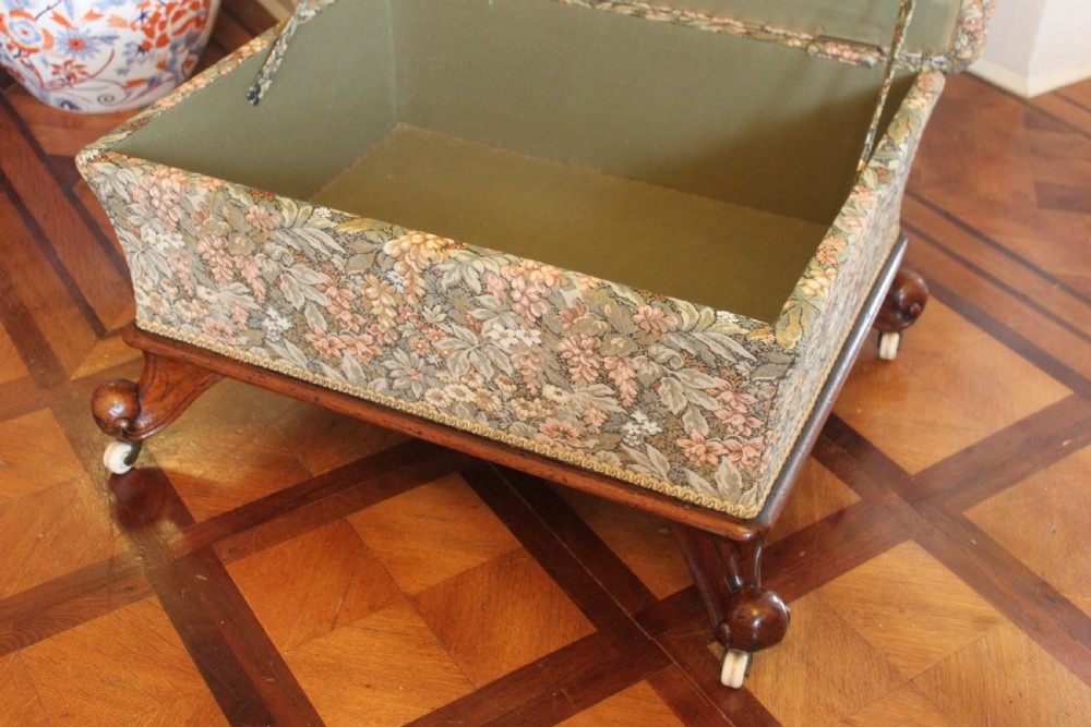 A square Victorian mahogany footstool upholstered in a beige, pink, and green floral tapestry pattern, supported by carved scroll legs with white ceramic castors. View VIII