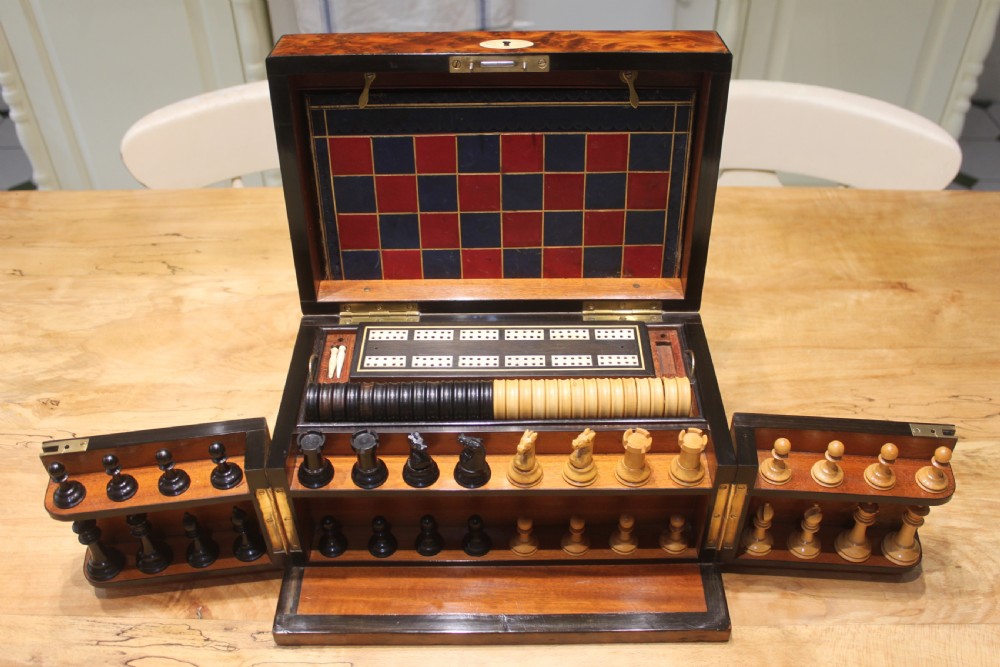 An opened Victorian burr walnut games compendium displaying wooden chess pieces, draughts, cribbage board, and an inlaid game board attached inside the lid. View II