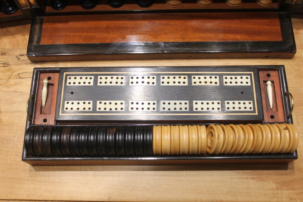 An opened Victorian burr walnut games compendium displaying wooden chess pieces, draughts, cribbage board, and an inlaid game board attached inside the lid. View V