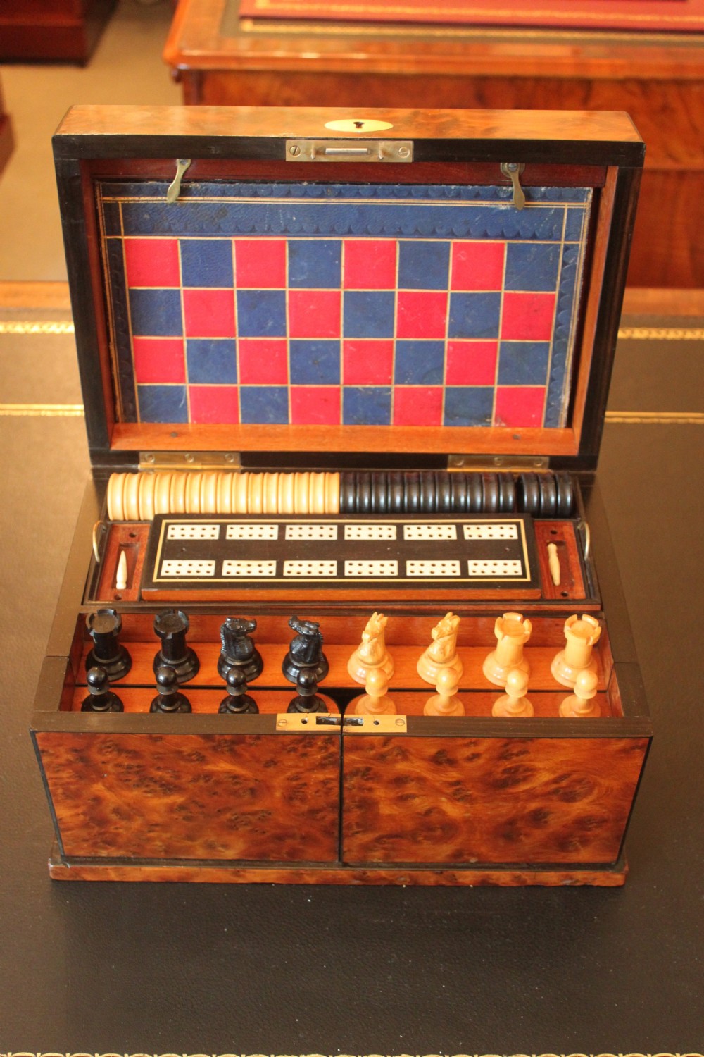 An opened Victorian burr walnut games compendium displaying wooden chess pieces, draughts, cribbage board, and an inlaid game board attached inside the lid. View X