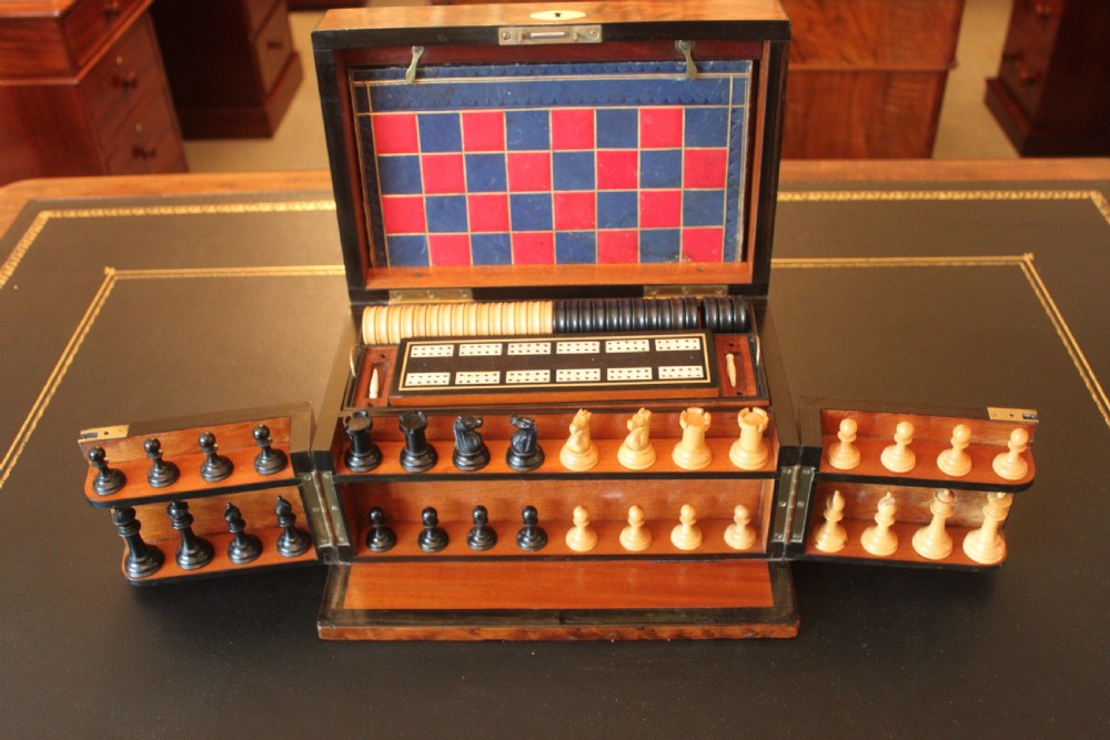 An opened Victorian burr walnut games compendium displaying wooden chess pieces, draughts, cribbage board, and an inlaid game board attached inside the lid.
