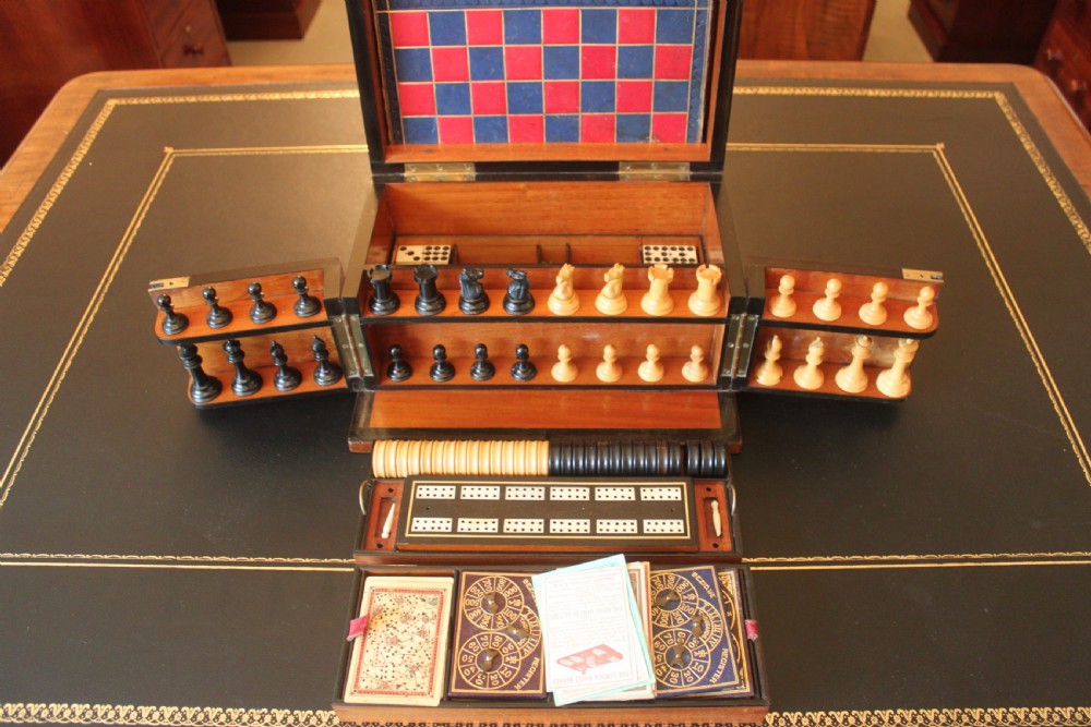 An opened Victorian burr walnut games compendium displaying wooden chess pieces, draughts, cribbage board, and an inlaid game board attached inside the lid. View XII