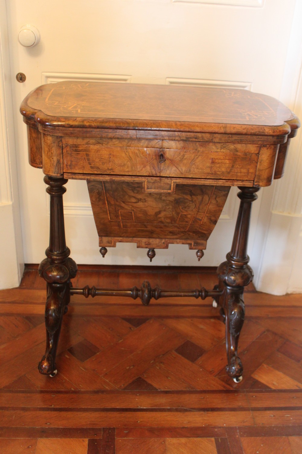 A Victorian burr walnut games and sewing table featuring inlay ornamentation, turned column supports, a wooden work well, and carved legs on castors.