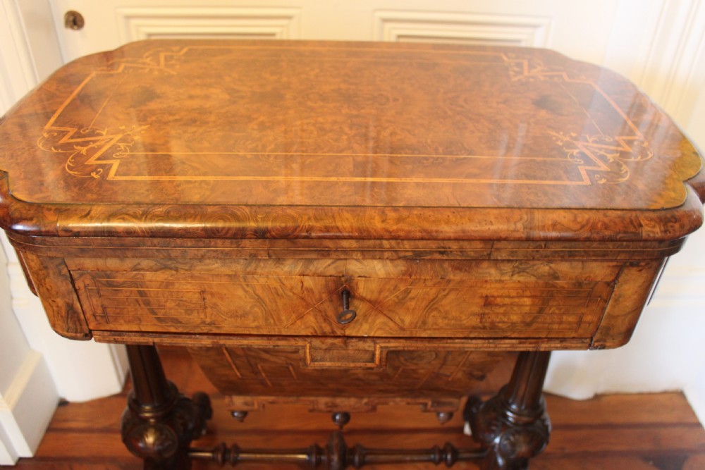 A Victorian burr walnut games and sewing table featuring inlay ornamentation, turned column supports, a wooden work well, and carved legs on castors. View III