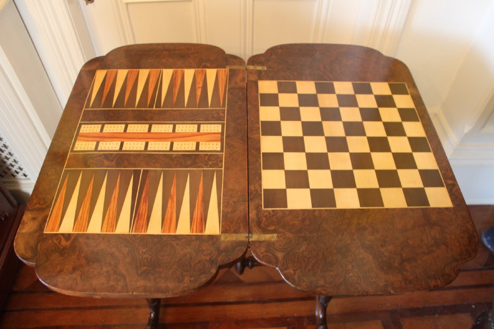 A Victorian burr walnut games and sewing table featuring inlay ornamentation, turned column supports, a wooden work well, and carved legs on castors. View VI