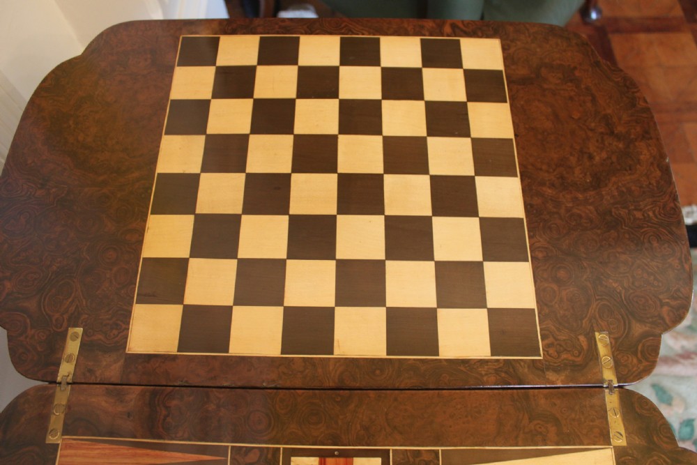 A Victorian burr walnut games and sewing table featuring inlay ornamentation, turned column supports, a wooden work well, and carved legs on castors. View VIII