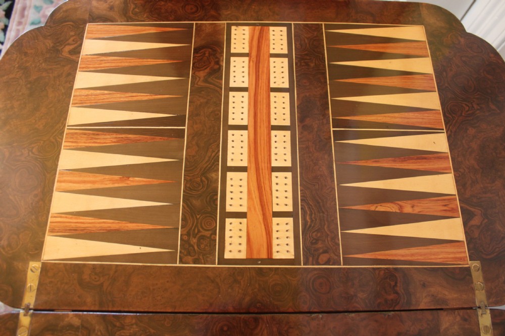 A Victorian burr walnut games and sewing table featuring inlay ornamentation, turned column supports, a wooden work well, and carved legs on castors. View IX