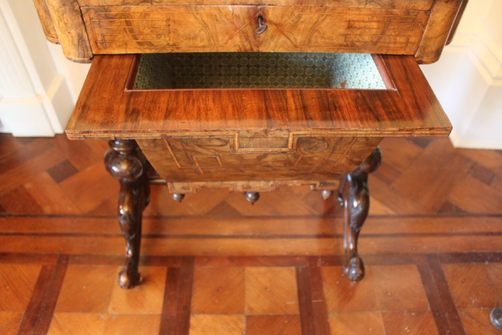 A Victorian burr walnut games and sewing table featuring inlay ornamentation, turned column supports, a wooden work well, and carved legs on castors. View X