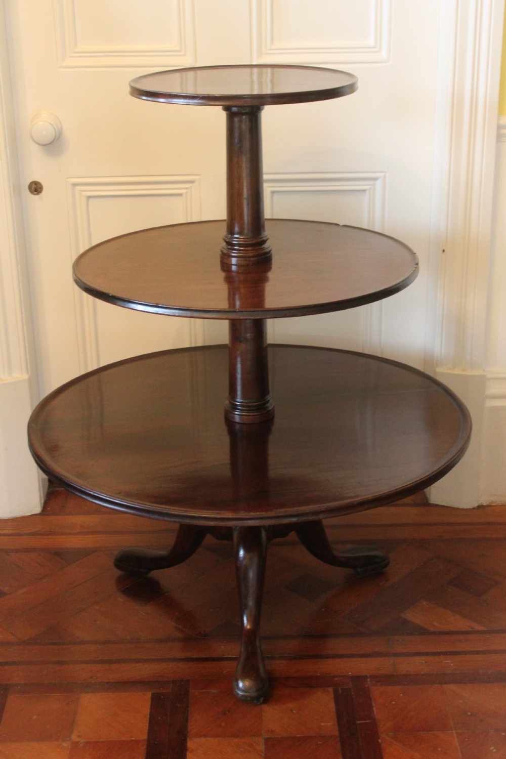 A three-tier Georgian mahogany dumb waiter featuring graduated revolving circular surfaces on a turned central column with a tripod base.