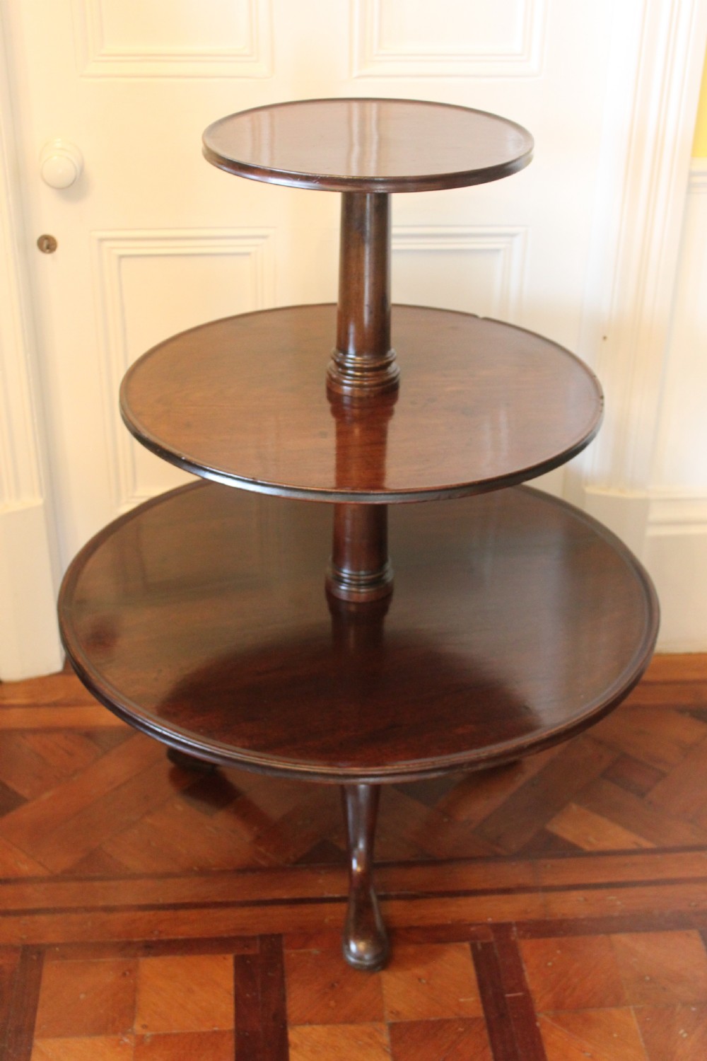 A three-tier Georgian mahogany dumb waiter featuring graduated revolving circular surfaces on a turned central column with a tripod base. View V