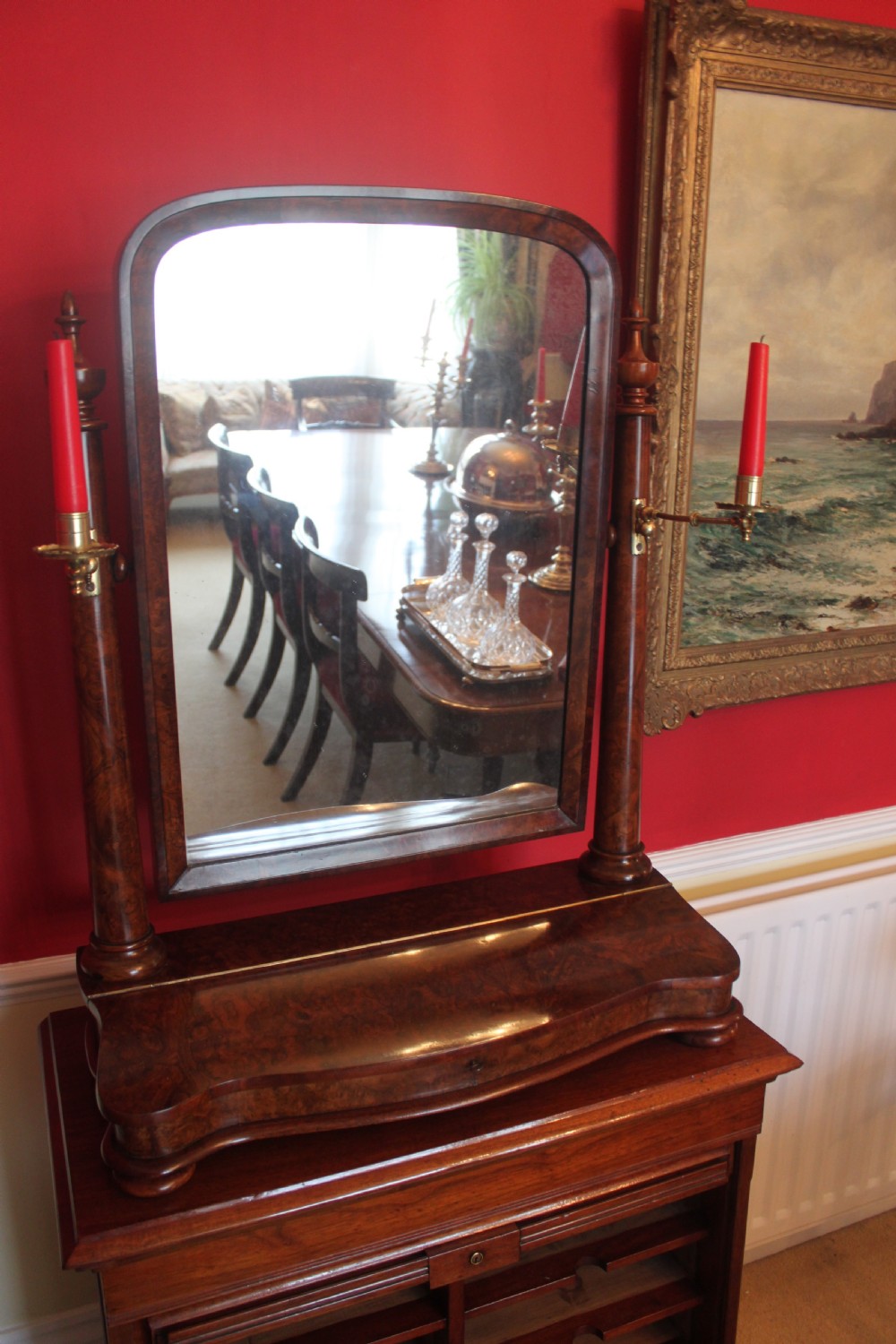 A Victorian burr walnut toilet mirror featuring a tilting arched glass frame set between turned columns with extended brass candle sconces on a shaped plinth base.