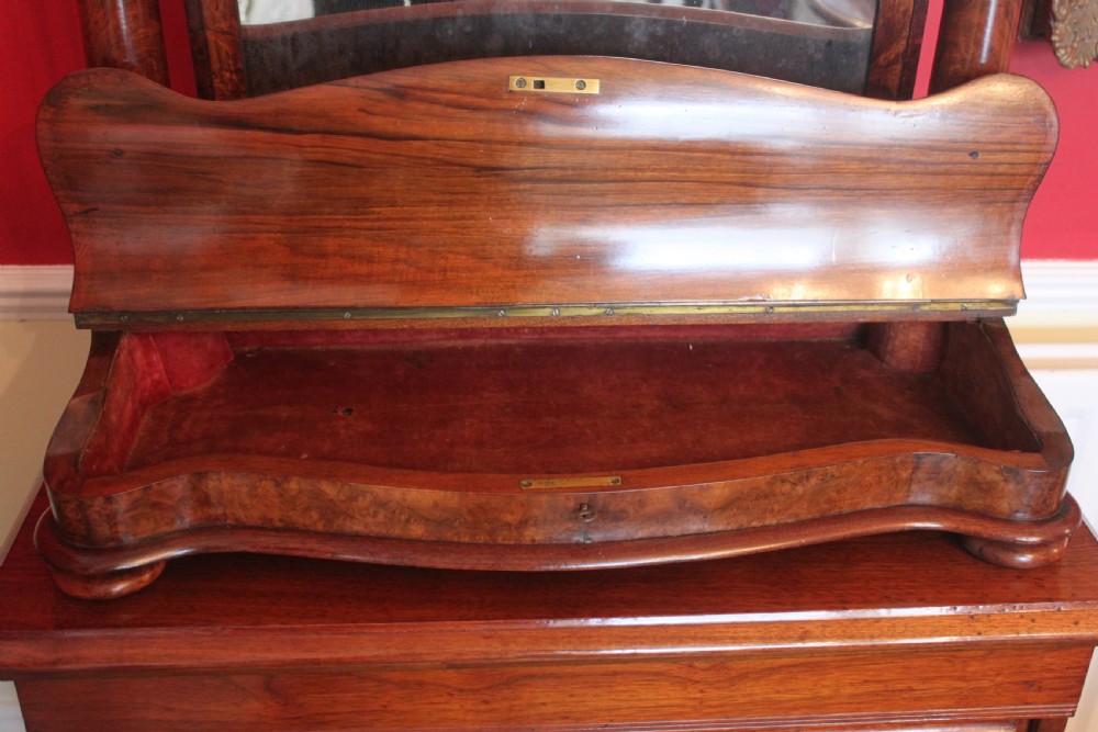 A Victorian burr walnut toilet mirror featuring a tilting arched glass frame set between turned columns with extended brass candle sconces on a shaped plinth base. View VI