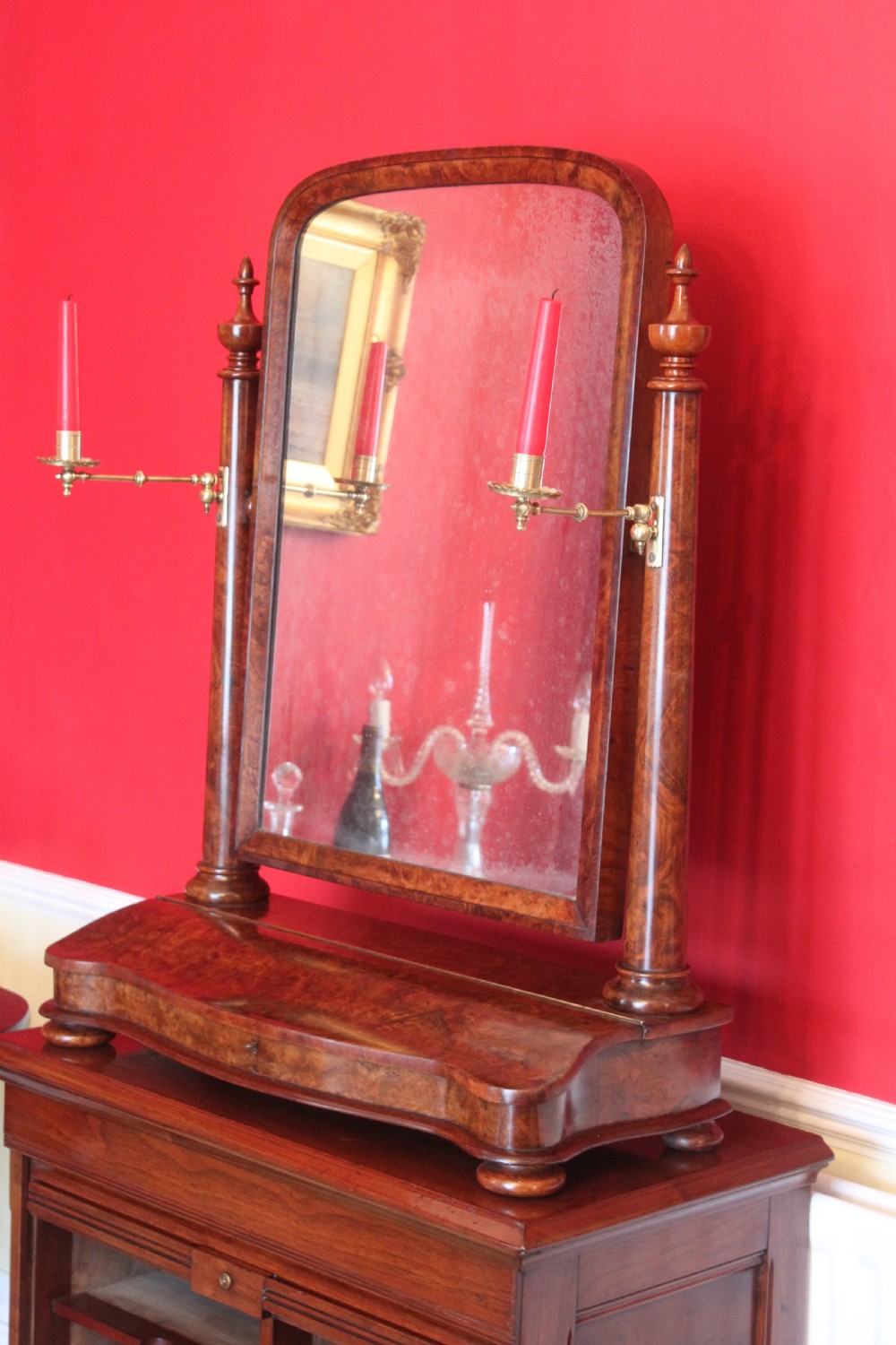 A Victorian burr walnut toilet mirror featuring a tilting arched glass frame set between turned columns with extended brass candle sconces on a shaped plinth base. View X