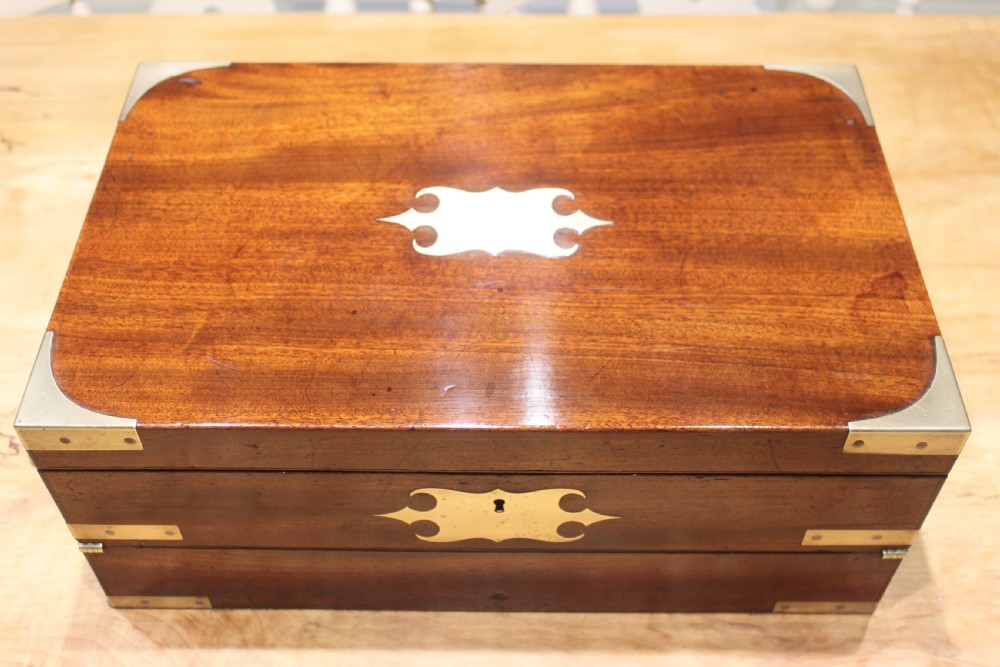 A closed rectangular late Georgian mahogany campaign writing slope featuring flush brass corner brackets, protective straps, and a decorative brass keyhole escutcheon. View II